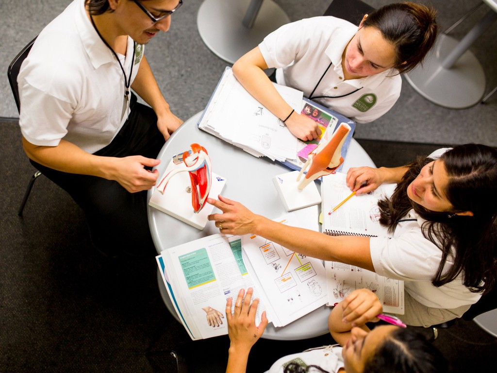 A cenital view of four students sitting around a table with pencils and study books at NHI massage school