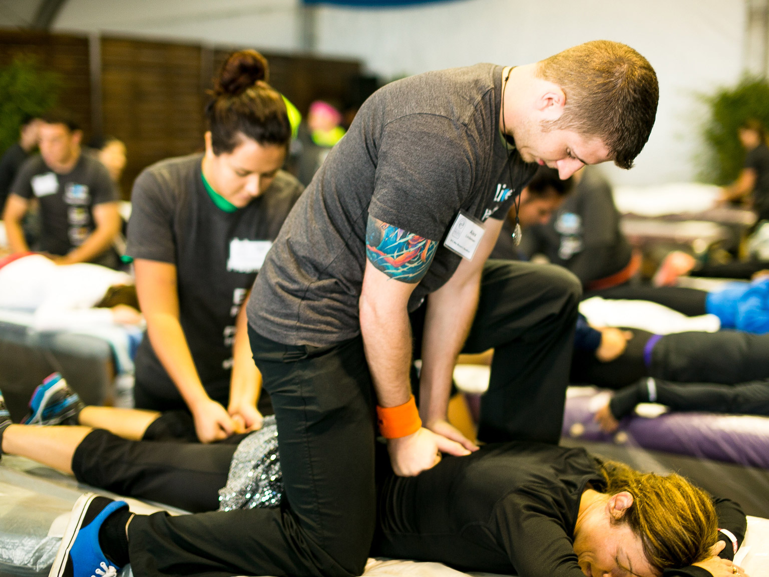 A man pressing his fists against the back of a person lying on a mat on the floor during a Sports Massage event at NHI Massage School